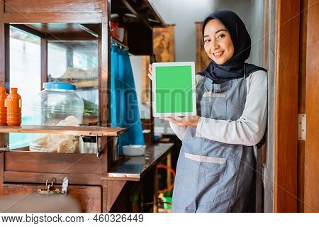 Veiled Woman Wearing Apron Smiling While Showing Tablet
