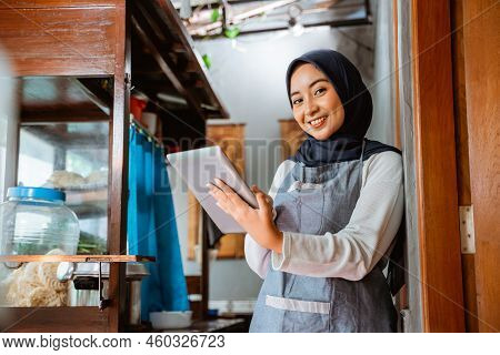 Woman In Veil Wearing Apron Smiling While Using Tablet Standing