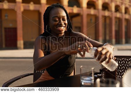 Young Black Woman Closing A Bottle Of Water While Resting In A Bar Terrace In The City