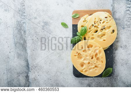Cheese Maasdam Or Radamer. Piece Of Cheese On Black Marble Or Stone Standa On Old Grey Concrete Back