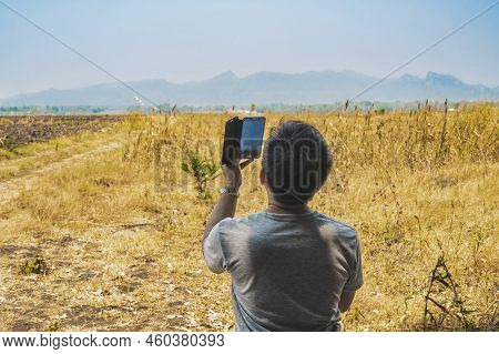 Male Farmer Use Cellphone To Take Picture Of Land To Make Farming Decisions In Field. Man Agricultur