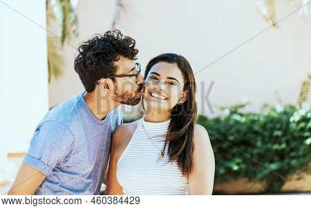 Boyfriend Kissing His Girlfriend On The Cheek While Smiling. Young Man Kissing His Girlfriend On The
