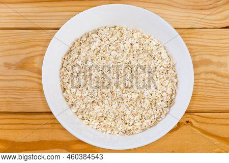 Raw Thin-rolled Oats In The White Bowl On A Rustic Table, Top View