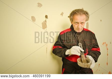 Older Man Working In Empty Apartment Repairing Holes In Walls