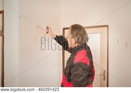 Older Man Removing Old Wallpapers Off The Walls In Empty Apartment