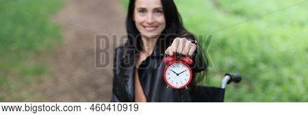 Smiling Woman In Wheelchair Holding Alarm Clock In Park. Part-time Work For Disabled