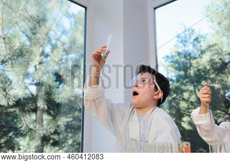 Caucasian Smart Nerd Schoolboy In Protective Goggles And White Lab Coat Holds A Test Tube With Green