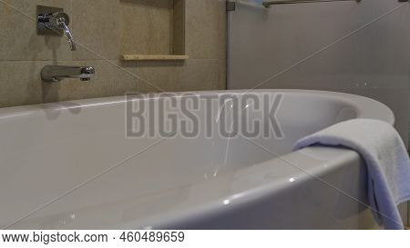 Large Acrylic Bathtub. Close-up. Shiny Chrome Faucet, Tile Wall. There Is A Folded White Towel On Th