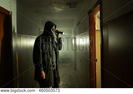 Man In Respirator Gas Mask With Flashlight Inside Of Abandoned Building In Dark. Cyberpunk Postapoca