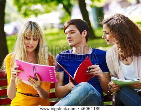 Estudiante feliz de grupo con el cuaderno en el banco al aire libre.