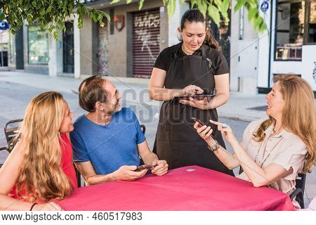Mature Group Order Food In Restaurant. Waitress Using Smartphone And Tablet Application Technology