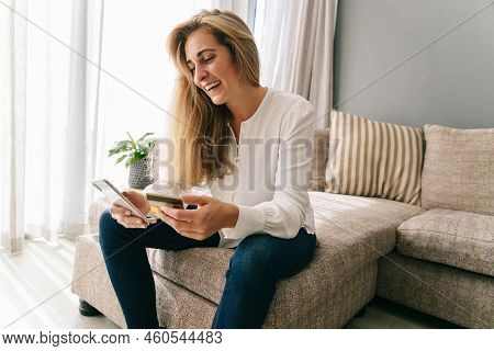 Cheerful Caucasian Mid Adult Woman With Blond Hair Using Smartphone And Credit Card For Online Shopp
