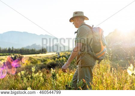 Mature Male Hiker With Backpack And Hat Walking Amidst Plants Against Clear Sky And Exploring Nature