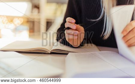 Midsection Of Young Female Student Holding Pen And Reading Textbooks While Doing Research On Desk In