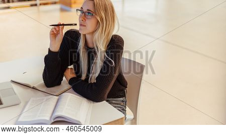 High Angle View Of Thoughtful Young Female Student Looking Away While Sitting With Textbook At Table
