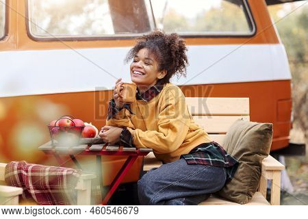 Young African American Woman Sitting At Table Near Car In Autumn Forest And Drinking Hot Tea, Dreamy