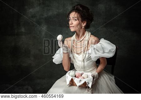 Young Adorable Girl In Image Of Medieval Royal Person Or Viscountess Tasting Sweets Isolated On Dark