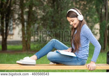 Concept Of Audiobook. Happy Teenage Girl Reading And Listening To Audiobook In Headphones, Audiobook