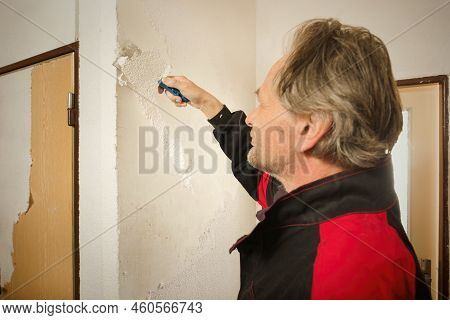 Older Man In Overall Removing Old Wallpapers In Apartment Room
