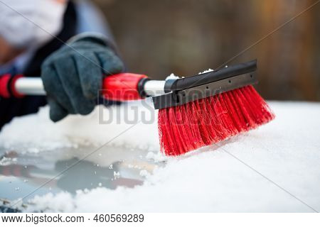 Man In Gloves Removing Snow From A Roof Of A Car With Red Brush