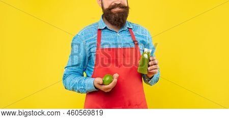 Happy Man Crop View In Red Apron Holding Limes And Juice Bottle Yellow Background, Juicery