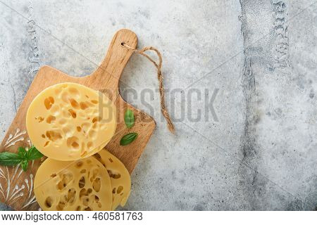 Cheese Maasdam Or Radamer. Piece Of Cheese On Wooden Standa On Old Grey Concrete Background. Top Vie