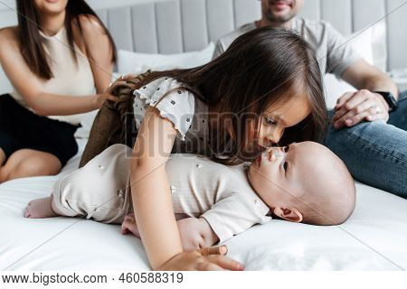 Young Parents And Their Children Play In Bed In A Bright Bedroom. Dad, Mom, Daughter And Newborn Bab