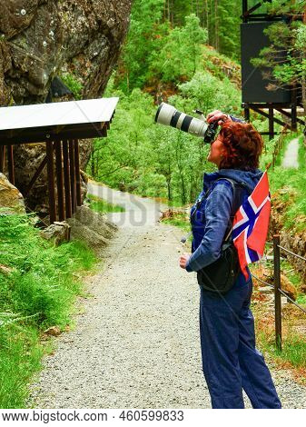 Tourist Woman With Norwegian Flag And Camera Taking Travel Picture, Walking Trough Mountains Path In