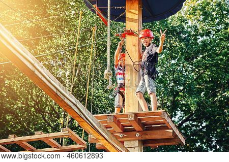 Brothers Junior Schoolchildren Spend Time In Rope Park In Summer Evening. Younger Brother Strengthen