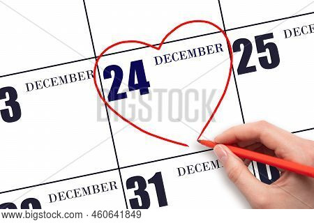 24th Day Of December. A Woman's Hand Drawing A Red Heart Shape On The Calendar Date Of 24 December. 