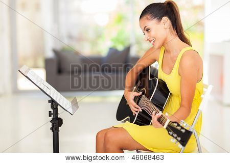 smiling pretty young woman playing guitar at home