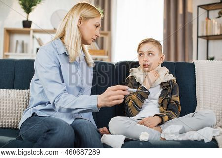 Mother Taking Care Of Her Cute Sick Teen Boy Suffering From Cold, Checking Temperature, Looking Each