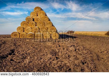 A Pile Of Straw Bales In The Shape Of A Pyramid, Stacked In A Plowed Field