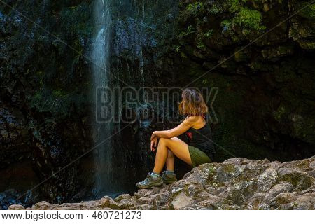 A Young Woman Looking At The Impressive Waterfall At The Levada Do Caldeirao Verde, Queimadas, Madei