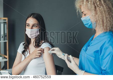 Young Female Nurse In Medical Face Mask And Gloves Holding Syringe And Giving Female Patient Flu Vac