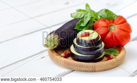 Eggplant, Tomato And Fresh Basil On A Wooden Plate On A White Background With Copy Space. Ingredient