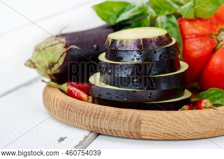 Slices Of Raw Eggplant With Drops, Close-up. Fresh Vegetables And Herbs On A Wooden Plate.
