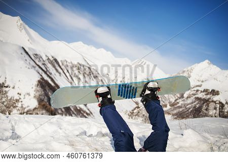 Guy In Jumpsuit Falls On Snowboard On Top Of Snowy Mountains