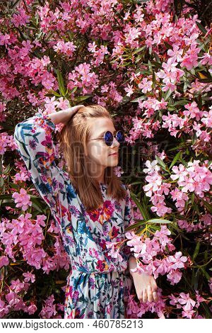Young Woman Stands In Beautiful Pink Flowers. Girl In A Colorful Linen Dressyoung Woman Stands In Be