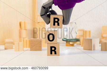 Ror The Word On Wooden Cubes, Cubes Stand On A Reflective Surface, In The Background Is A Business D