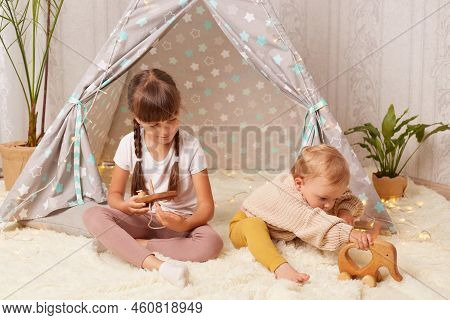Portrait Of Charming Friendly Little Sisters Playing In Peetee Tent With Wooden Toy, Children Sittin