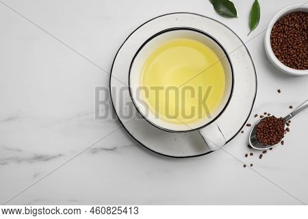 Cup Of Buckwheat Tea And Granules On White Marble Table, Flat Lay. Space For Text
