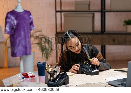 African American Designer Painting On Shoe Near Gadgets And Sewing Pattern.