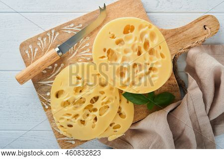 Cheese Maasdam Or Radamer. Piece Of Cheese On Wooden Stand Board On White Wooden Table Background. T
