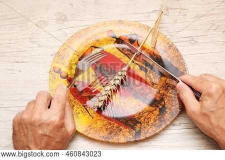 On A Plate With African Patterns Is A Grain Ear, In The Hands Of A Fork And A Knife. A Symbol Of Hun