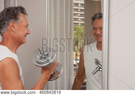Mature Man 60plus Working Out With Weights At Home In Front Of A Mirror Doing Bicep Curls