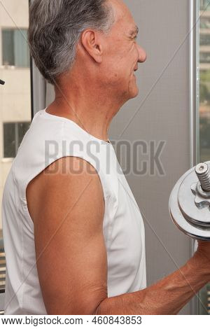 Mature Man 60plus Working Out With Weights At Home In Front Of A Mirror Doing Bicep Curls