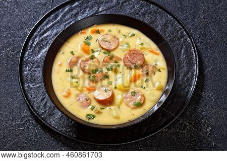 Kartoffelsuppe, German Potato Soup With Sausages In Black Bowl On Dark Table, Horizontal View From A