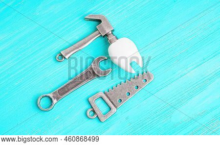 Human Tooth Model, Steel Hammer, Wrench And Handsaw On A Blue Wooden Background With Copy Space. Cho