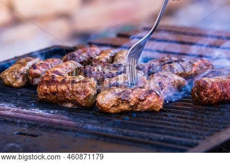 Preparing Meat Rolls Called Mici Or Mititei On Barbecue. Close Up Of Grill With Burning Fire With Fl